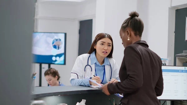 African American Receptionist Asian Doctor Working Reception Counter Filling Report — Stock Fotó