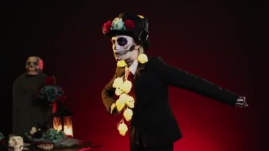 Stüdyoda ölüm kostümü giymiş, kulaklıkla müzik dinleyen ve dans hareketleri yapan korkunç bir kadın. Dios de los muertos 'u kutlamak için kutsal Meksika tanrıçasına benziyor. El kamerasıyla..