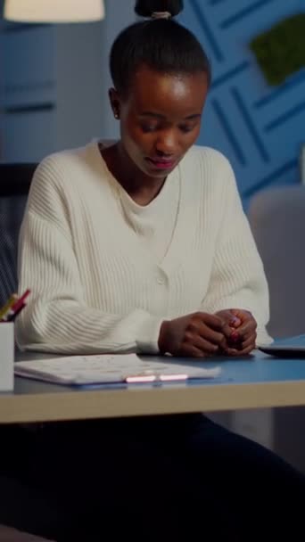 深夜にスタートアップ金融会社で働くノートパソコンからカメラを見て微笑む黒人女性の姿 プロジェクトの締め切りを尊重する残業を行う集中従業員 — ストック動画