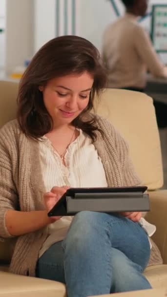 经理女士在平板电脑上搜寻时 坐在舒适沙发上的放松区微笑着 指着笔记本微笑着 而不同的同事则在幕后工作 规划财务项目的同事 — 图库视频影像