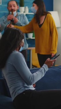 Dikey video: Afrikalı kadın akıllı telefonda komik bir klip gösteriyor. Evde takılıyor, maske takıyor ve küresel salgın sırasında koronavirüsü önlüyor. Sosyal mesafeyi koruyor, partiden keyif alıyor.