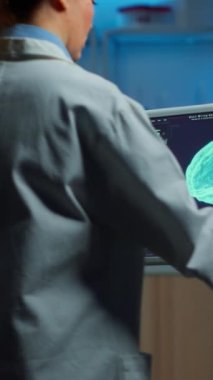 Dikey video: Nörolog doktor hastanın beyin taramasına baktığını ve hastanın beyin taramasını analiz ettiğini ve EG kulaklık taktığını söylüyor. Bilim adamı sinir sistemini inceleyen notlar alıyor.