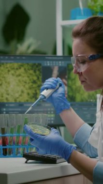 Dikey video: Kimyager kadın test tüpünden mikro pipetle DNA sıvısı alıyor ve petri kabına genetik mutasyonu analiz ediyor. İlaç laboratuarında çalışan biyolog araştırmacısı.
