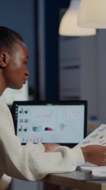 Elinde grafik ve mali istatistikleri olan Afrikalı bir iş kadını dizüstü bilgisayarın önünde çalışıyor ve yeni açılan iş ofisinde oturuyor. Projenin bitiş tarihine göre odaklanmış çalışan