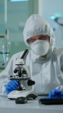 Dikey video: Ekipmanlı laboratuvarda mikroskop üzerinde DNA örneklerini kontrol eden biyolog doktor. Yüksek teknoloji ve kimya araçları kullanılarak tıbbi laboratuarda aşı evrimi inceleniyor.