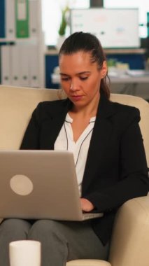 İspanyol iş kadını, arka planda çalışan çeşitli meslektaşlar çalışırken koltukta oturup bilgisayarla yazı yazarken kameraya gülümsüyor. Modern ofisteki başlangıç mali raporlarını analiz eden çok ırklı iş arkadaşları