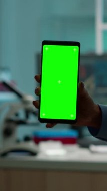 Dikey video: Hemşire kan örnekleri getirirken, kimyagerlerin elinde yeşil ekranlı akıllı telefonu tutan kimyagerleri kapatın. Bilim adamı akıllı telefon kullanıyor. Model, krom anahtar.