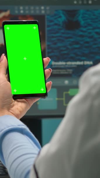 垂直ビデオ 現代の設備の整った研究室で緑のモックアップと携帯電話を見て微生物学者の医師の女性のバックビュー クロマキーを用いたワクチン研究を行う科学者チーム — ストック動画