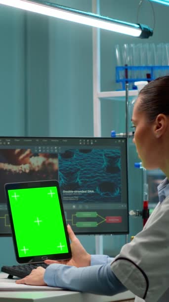垂直视频 微生物学家在配备绿色彩色键显示的现代实验室的记事本上工作 生物技术科学家小组开发使用模拟屏幕平板药物 — 图库视频影像