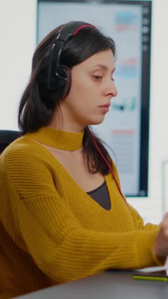 スタイラスペン コーヒーを飲み 2つのディスプレイでPc上で作業を使用して ヘッドフォンのレタッチ画像を持つフォトエディタ クリエイティブ代理店に座ってグラフィックタブレットとソフトウェアアプリで女性のレタッチ編集 — ストック動画