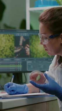 Dikey video: Biyolog kadın mikrobiyoloji laboratuvarında çalışan vejetaryen etli et kabını elinde tutarken tıbbi uzmanlık yazıyor. Gıda araştırması yapan kimyager kadın genetiği değiştirilmiş.