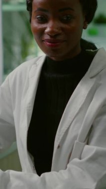 Dikey video: Mikrobiyoloji laboratuvarında dikilirken kameraya bakan beyaz önlüklü bir biyolog kadının portresi. Uzman ekip genetik mutasyonu araştırıyor.