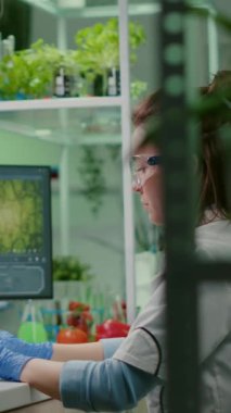 Dikey video: Mikrobiyoloji deneyi için bilgisayarda biyokimya uzmanı olan bilim kadını araştırmacısı. İlaç laboratuarında çalışan tıbbi ekip genetik mutasyonu analiz ediyor.