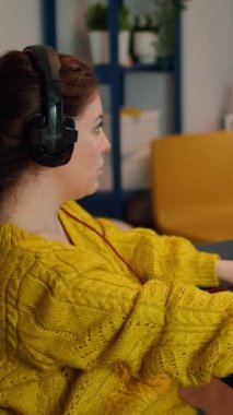 Dikey video: Kadın oyuncu kameraya bakarak ana koltuktan havalanıyor, gülümsüyor ve sanal ortamda sanal atıcılık oyunu şampiyonasında oynuyor, esport oyuncuları oyun sırasında bilgisayar üzerinde performans sergiliyorlar