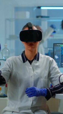 Dikey video: Laboratuvarda tıbbi yenilik kullanarak sanal gerçeklik gözlüğü takan profesyonel bilim adamı. Ekip araştırmacıları ekipman aygıtı, gelecek, tıp, sağlık, profesyonel