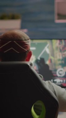 Dikey video: Profesyonel oyuncunun profesyonel güçlü bilgisayardaki yeni FPS video oyununun grafiklerini test edişinin arka görüntüsü. Sanal atıcılık oyunu siber uzayda oynanıyor, esports player oynanıyor