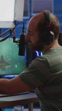 Dikey video: Profesyonel siber adam video oyunu yayınlıyor, canlı sohbette okuyor ve RGB güçlü bilgisayarında uzay nişancısı oynuyor. Oyun sandalyesinde oturmuş online esportlar sırasında oyun oynayan flamalar