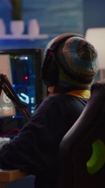 Dikey video: Profesyonel kulaklıklar kullanarak sanal rekabet için nişancı oyunu oynayan odaklanmış flamalar. Oyun turnuvası sırasında RGB ile birlikte güçlü PC kullanarak çevrimiçi yayın yapan siber performans.