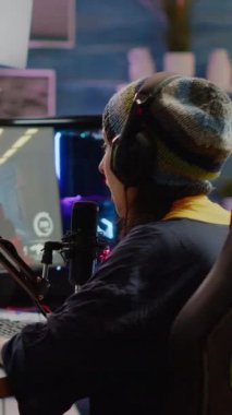 Dikey video: Pro streamer ses kontrol kulaklık takıyor ve sanal yarışma sırasında FPS video oyunu oynamaya başlıyor. Profesyonel akış ayarını kullanan oyuncu, oyun sırasında sohbet akışı