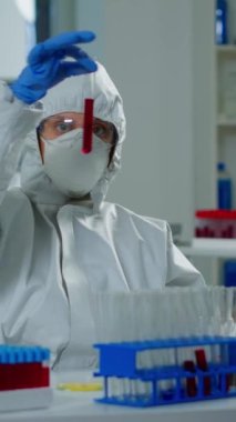 Dikey video: Tıp laboratuarında yeni bir tedavi için üzerinde kan örneği bulunan tüpler üzerinde çalışan araştırmacı. Aşı geliştirmek için yüksek teknoloji kullanan doktorlar virüs evrimini inceliyor.