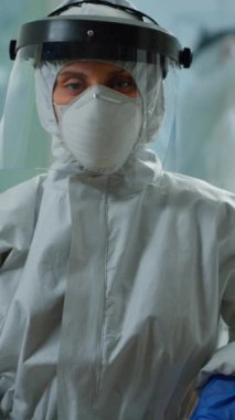Dikey video: Yorgun mikrobiyolog laboratuarda oturmuş kameraya bakıyor. Bilimsel araştırmalar için yüksek teknoloji ve kimya araçları kullanarak virüs evrimini inceleyen bilim adamları ekibi