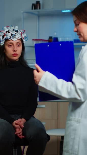 垂直视频 神经科学医生拿着剪贴板 向脑病患者展示治疗方法 如耳机 神经科学实验室治疗神经系统的妇女 — 图库视频影像