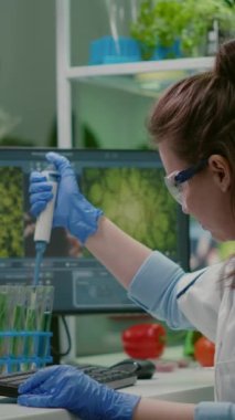 Dikey video: Biyolog bilim adamı mikro pipetle test tüpüne çözelti sıvısı koyuyor ve tıbbi uzmanlığı kullanıyor. Beyaz önlüklü kadın araştırmacı profesyonel mikrobiyoloji laboratuvarında çalışıyor.