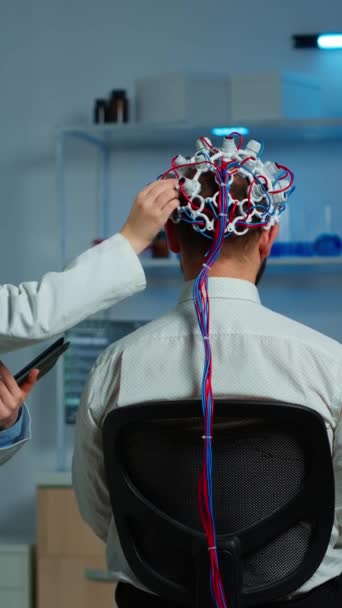 垂直ビデオ 医療研究者が神経系を制御しながら 神経研究室での脳電気活動をスキャンし 神経系を調べる高性能Egヘッドセットを身に着けている患者 — ストック動画