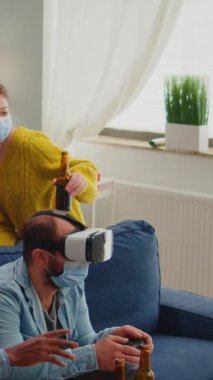 Dikey video: Coronavirus enfeksiyonunu önlemek için oturma odasında video oyunu oynayan çok ırklı arkadaşlar sosyal mesafeyi korumak amacıyla maske takıyorlar. Çeşitli insanlar eğleniyor.
