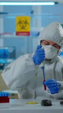 Dikey video: Pen kıyafetli bilim teknisyeni mikro pipet ve petri kabını kullanarak laboratuvarda kan tahlili yapıyor. Aşı geliştirmek için virüs evrimini inceleyen ekip