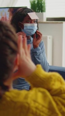 Dikey video: Alnında isim oyunu oynayan, bira içen ve popcronla eğlenen insanların karışık ırkı sosyal acıyı devam ettiriyor. Evde kovid19 yayılmasını önlemek için yüz maskesi takıldı.