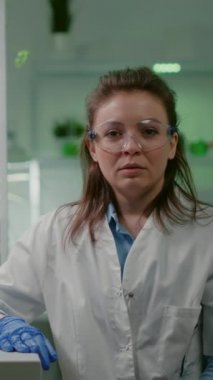 Dikey video: Botanik bilim laboratuvarında otururken biyolog ekibiyle birlikte analiz yapan tıbbi ekipmanlı bir kadın biyolog. Uzmanlar araştırıyor