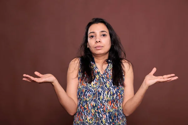 Confused indian woman shrugging shoulders with questioning facial expression portrait. Puzzled lady standing with hands spread wide, doubting, pensive person looking at camera