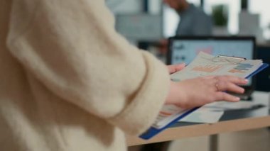Closeup of woman hands holding clipboard with papers looking at pie chart and business profit data in startup office. Focused employee analyzing key performance indicators reading turnover statistics.
