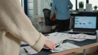 Seçici odak noktamız tableti tutan kadınların ellerinin satış grafiğine yakınlaşması ve verileri dizüstü bilgisayardaki istatistiklerle karşılaştırması. Ofisteki dijital aygıtla çalışan çalışanların kapatılması.