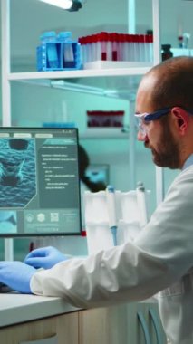 Dikey video: Doktorun bilgisayarda yazı yazması yıpranmış ve gece geç saatlerde donanımlı laboratuvarda kameraya yorgun görünüyor. Tıbbi kimyagerler, bilimsel araştırmalar için yüksek teknoloji kullanarak virüs evrimini inceliyorlar.