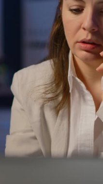 Dikey video: Gece geç saatlerde iş yerinde fazla mesai yaparken telefonla konuşan yorgun serbest çalışan kadın. Modern teknoloji kablosuz ağıyla odaklanmış çalışan
