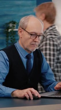 Dikey video: Ev yapımı kahve içerek çalışan eski girişimci dizüstü bilgisayardaki grafikleri kontrol ediyor. Emekli çalışan modern teknoloji kullanarak daktilo okuyor, araştırıyor.