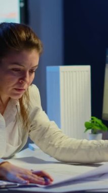 Dikey video: Aşırı çalışan kadın mimar, gece geç saatlerde bilgisayarın önünde oturmuş planları analiz ediyor ve eşleştiriyor. Fazla mesai yapan binaların mimari planlarını kullanan tasarımcı