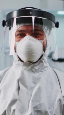 Dikey video: Modern donanımlı laboratuvarda kameraya gülümseyen, üstü örtülü bilim adamının portresi. Kimyager doktor virüs evrimini bilimsel araştırmalar için yüksek teknoloji kullanarak xamining