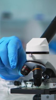 Dikey video: Pelerin giysisindeki mikroskop kullanarak virüsü analiz eden kimyager doktorunu kapatın. Aşı evrimini inceleyen bilim adamlarından oluşan bir ekip, tedavi geliştirme araştırmaları için yüksek teknoloji kullanıyor.