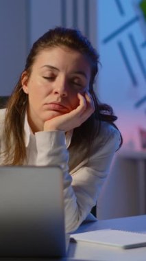 Dikey video: Uzaktan kumandalı bir kadın gece geç saatlerde dizüstü bilgisayarda çalışırken koltukta uyukluyor. Modern teknoloji ağını kablosuz kullanarak fazla mesai yaparak meşgul bir çalışan.