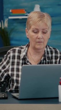 Dikey video: Evde dizüstü bilgisayarda çalışan orta yaşlı bir iş kadını, masada oturan bilgisayar verileri üzerinde yazan yaşlı olgun bir kadın. Emekli koca, modern teknolojiyi kullanan bir işçi.