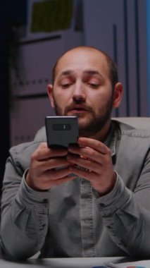 Girişimci telefonda gülümserken şirket ofisindeki masa başında oturan finansal strateji planlayıcısı. İş adamı gece geç saatlerde internette sosyal medya fikirlerini tarıyor
