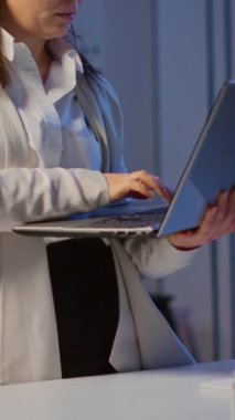 Dikey video: Yorgun bir iş kadını dizüstü bilgisayar tutuyor, daktilo çekiyor ve iç çekiyor. Çalışan teknoloji ağını kablosuz kullanarak fazla mesai yapıyor