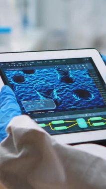 Dikey video: Koruyucu kıyafetli doktorun dijital tablete bakarak virüs evrimini analiz edişi. Aşı geliştirme çalışmaları yapan bilim adamları, tedavi için yüksek teknolojiyi kullanıyorlar.
