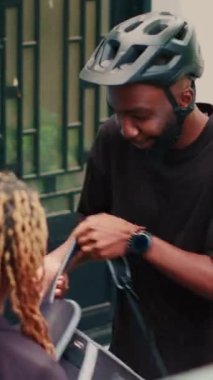 Dikey video: Kapıda kuryeyle servis edilen ekspres restoran teslimat servisi, müşterilere kese kağıdında yemek veriyor. Afro-amerikan müşteri hazır yemek paketinde, teslimat...