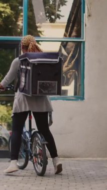 Dikey video: Restoran işçisi ön kapıdaki erkek müşteriye yemek siparişi veriyor. Afro-Amerikan kuryesi, restoranın girişindeki adama yemek servisi yapıyor.