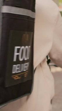 Dikey video: Yemek servisi çalışanı sırt çantası taşıyor ve bisiklete biniyor, termal çanta içinde fast food siparişi veriyor. Bisikletli teslimatçı. Restoran teslimatı.