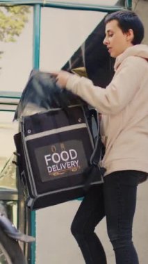 Dikey video: Restoran servisi müşterisi fast food siparişini kredi kartıyla ödüyor, kadın kurye postal terminalini tutuyor. Müşteri postacıdan yiyecek paketi almak için bağlantısız ödeme yapıyor..